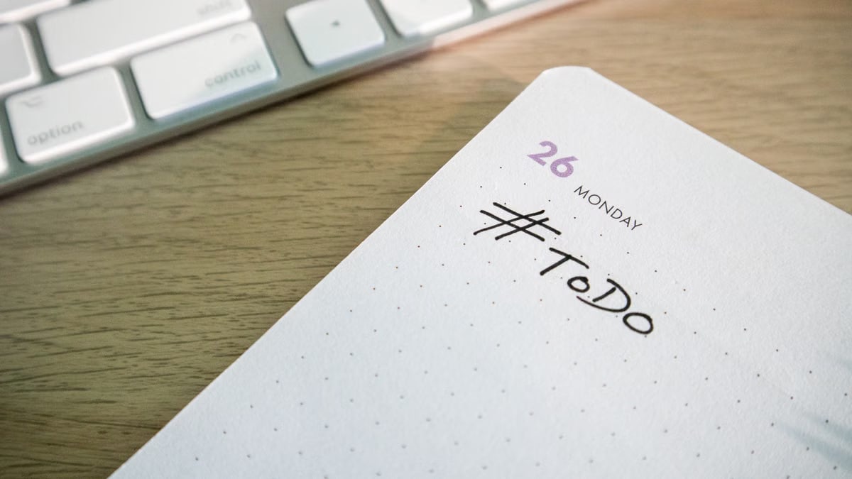 Close-up of a to-do list next to a computer keyboard on a desk.